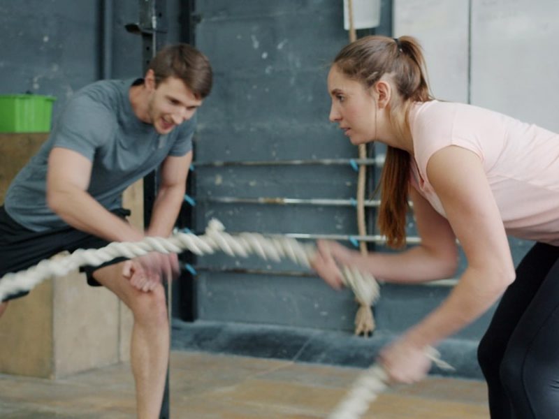Portrait of young attractive sportswoman exercising with battle ropes in gym with support of sports trainer handsome guy in sportswear. People and sports concept.