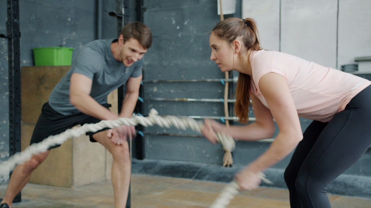 Portrait of young attractive sportswoman exercising with battle ropes in gym with support of sports trainer handsome guy in sportswear. People and sports concept.